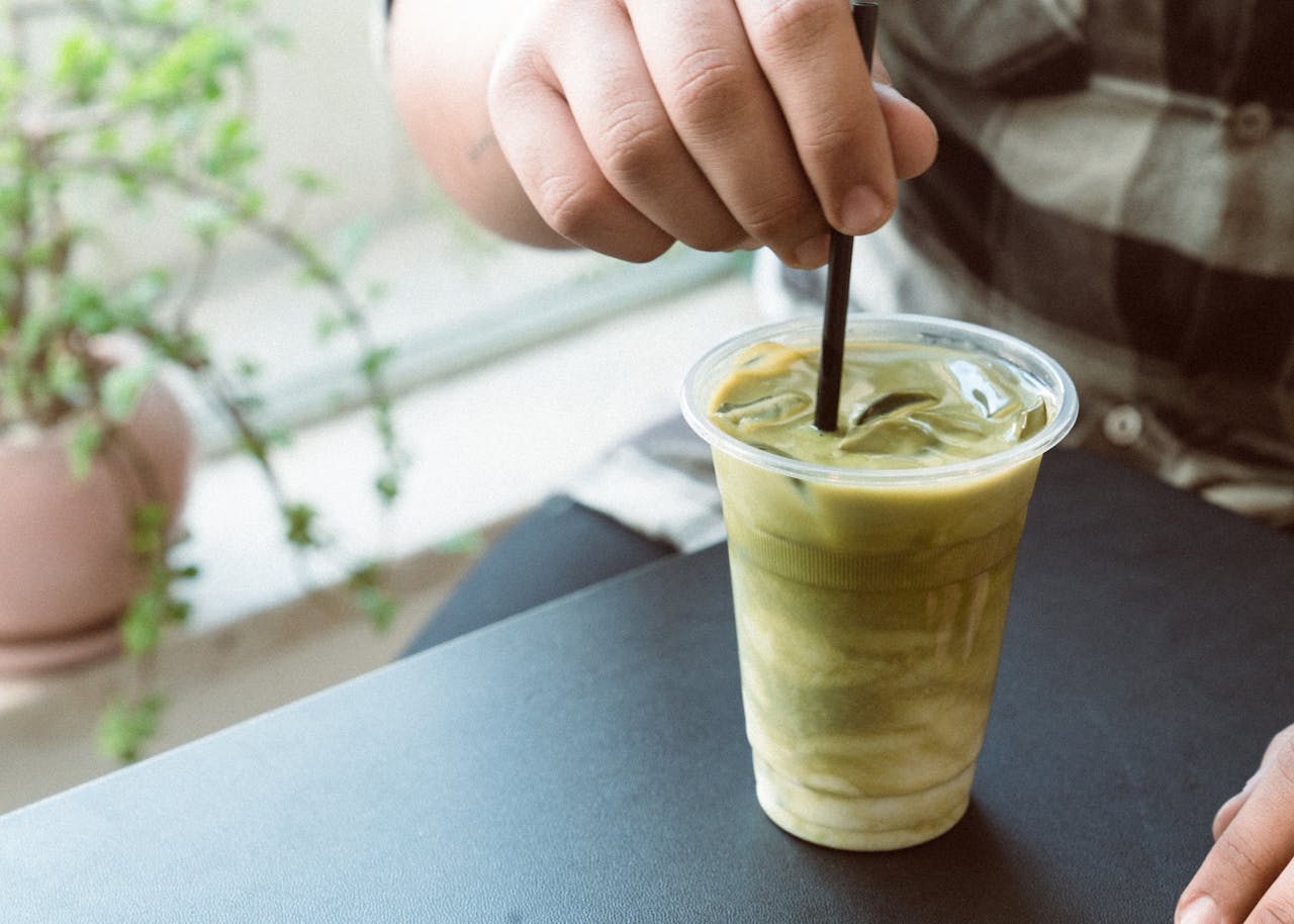 Hand stirring an iced matcha latte at a cozy café, perfect for a refreshing break.