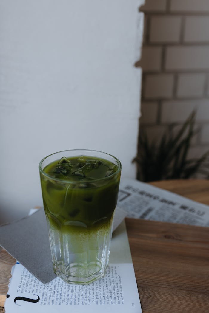 A glass of iced matcha latte with ice cubes on a wooden table, creating a relaxed vibe.