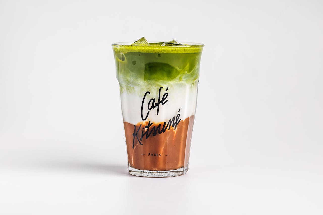 Colorful iced matcha latte in a Cafe Kitsune branded glass cup, artfully layered.