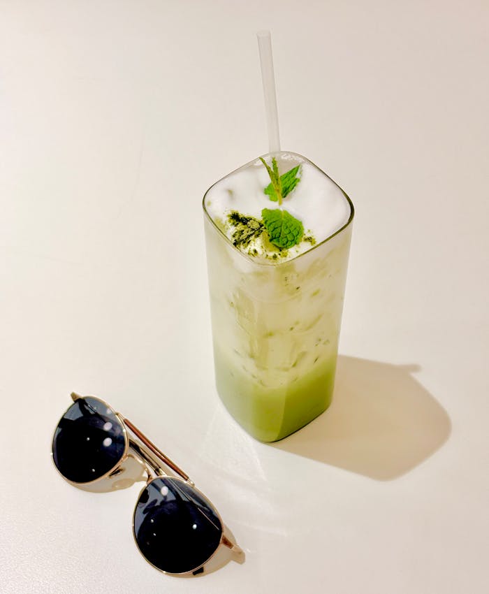 Iced matcha latte with mint garnish and sunglasses on a sunny day.