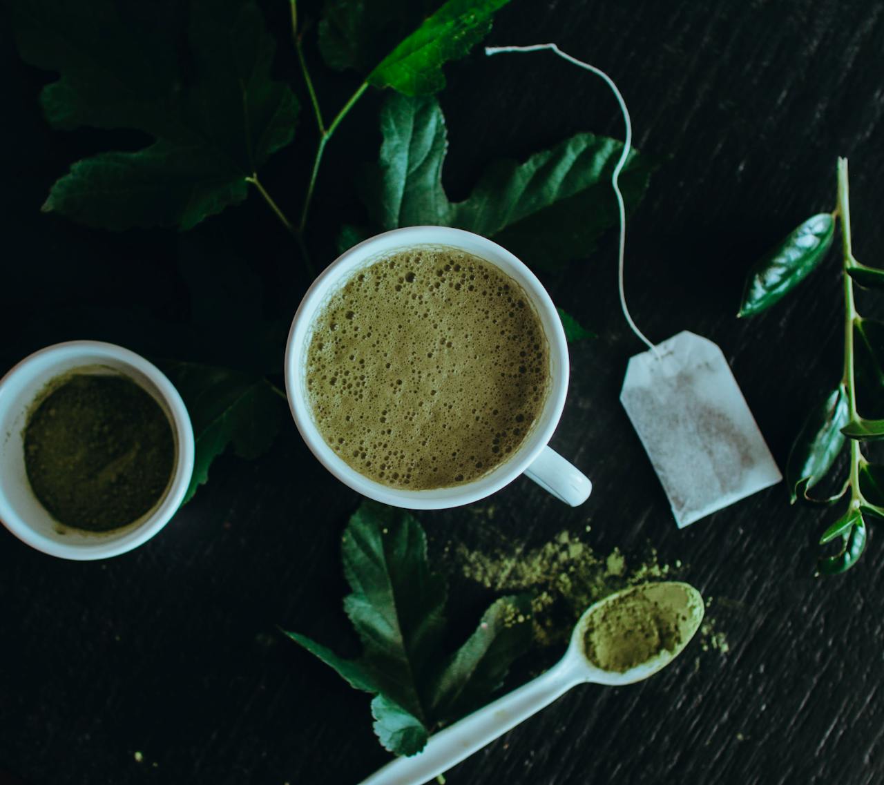 Top view of a refreshing matcha latte surrounded by leaves, powder, and a tea bag.